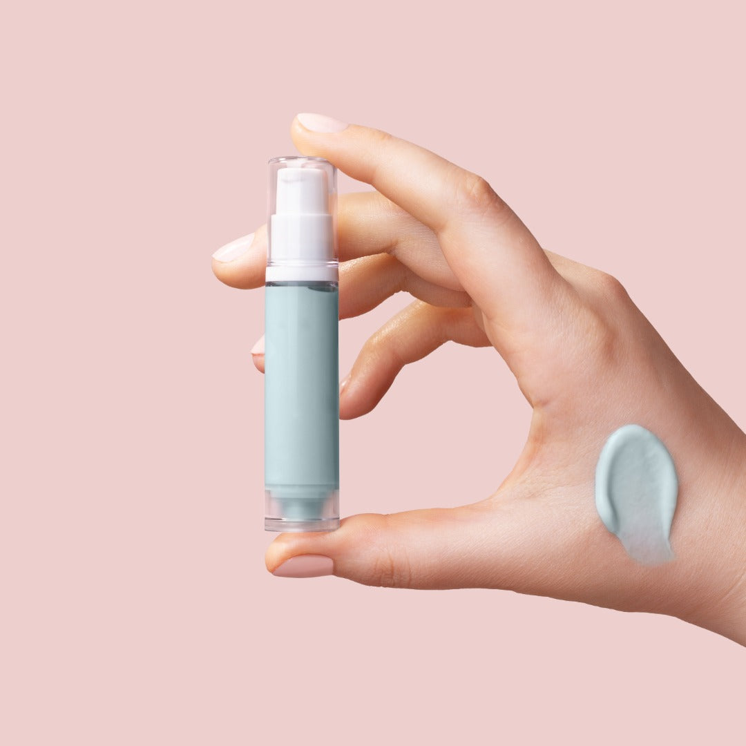 Hand holding a small skincare bottle with a sample on a pink background
