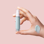 Hand holding a small skincare bottle with a sample on a pink background