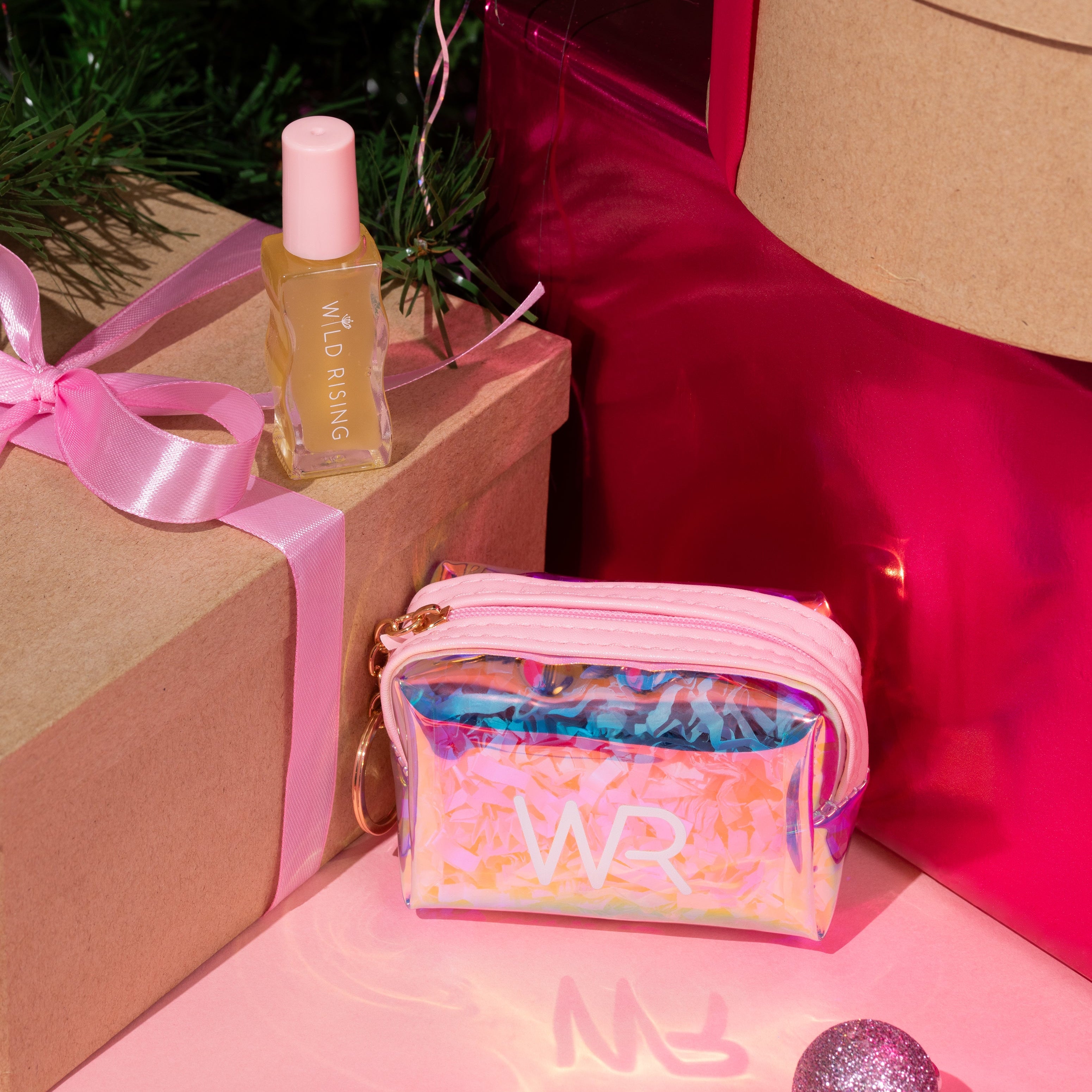Gifts under a decorated Christmas tree with a pink bag and bottle.