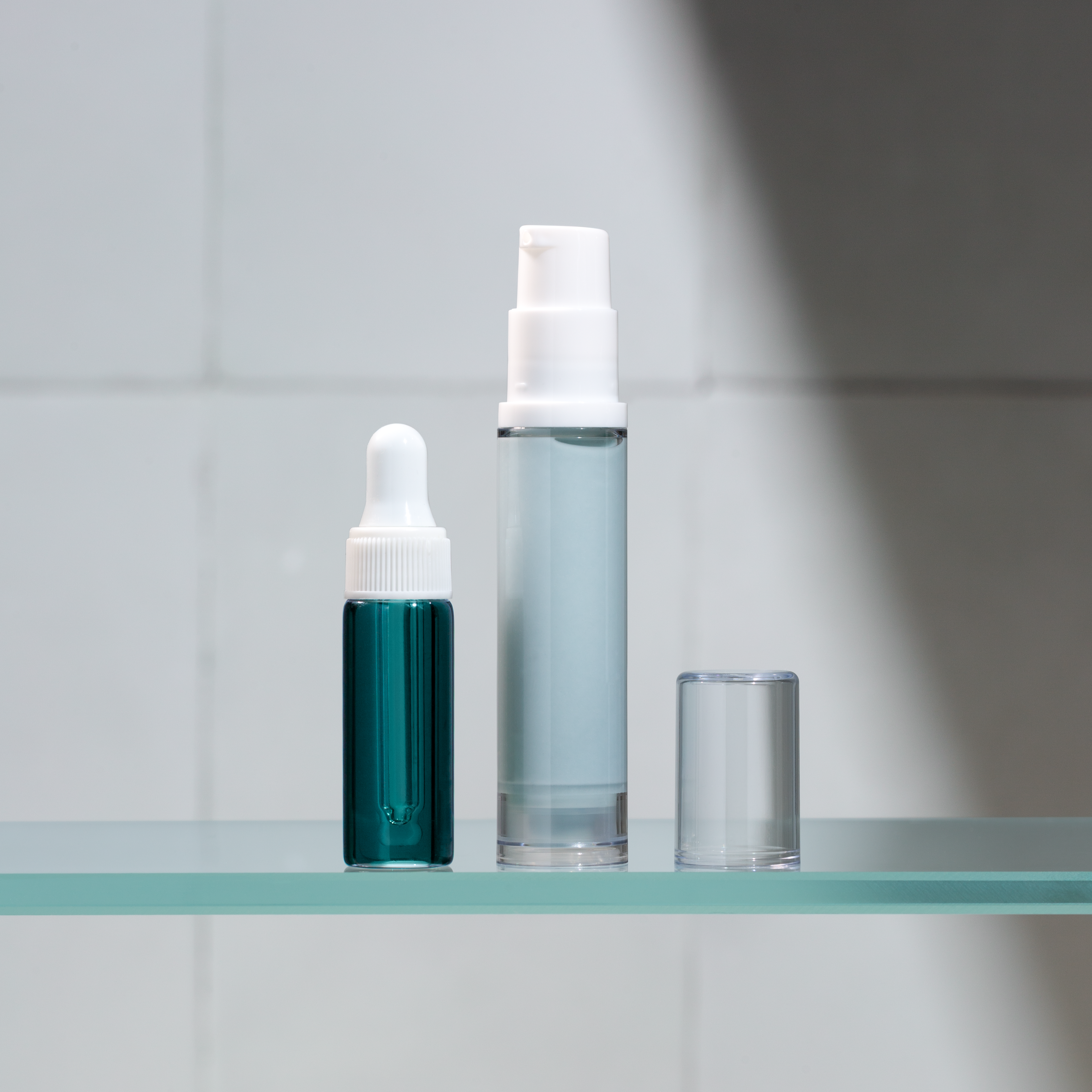 Two skincare bottles on a glass shelf with a neutral background