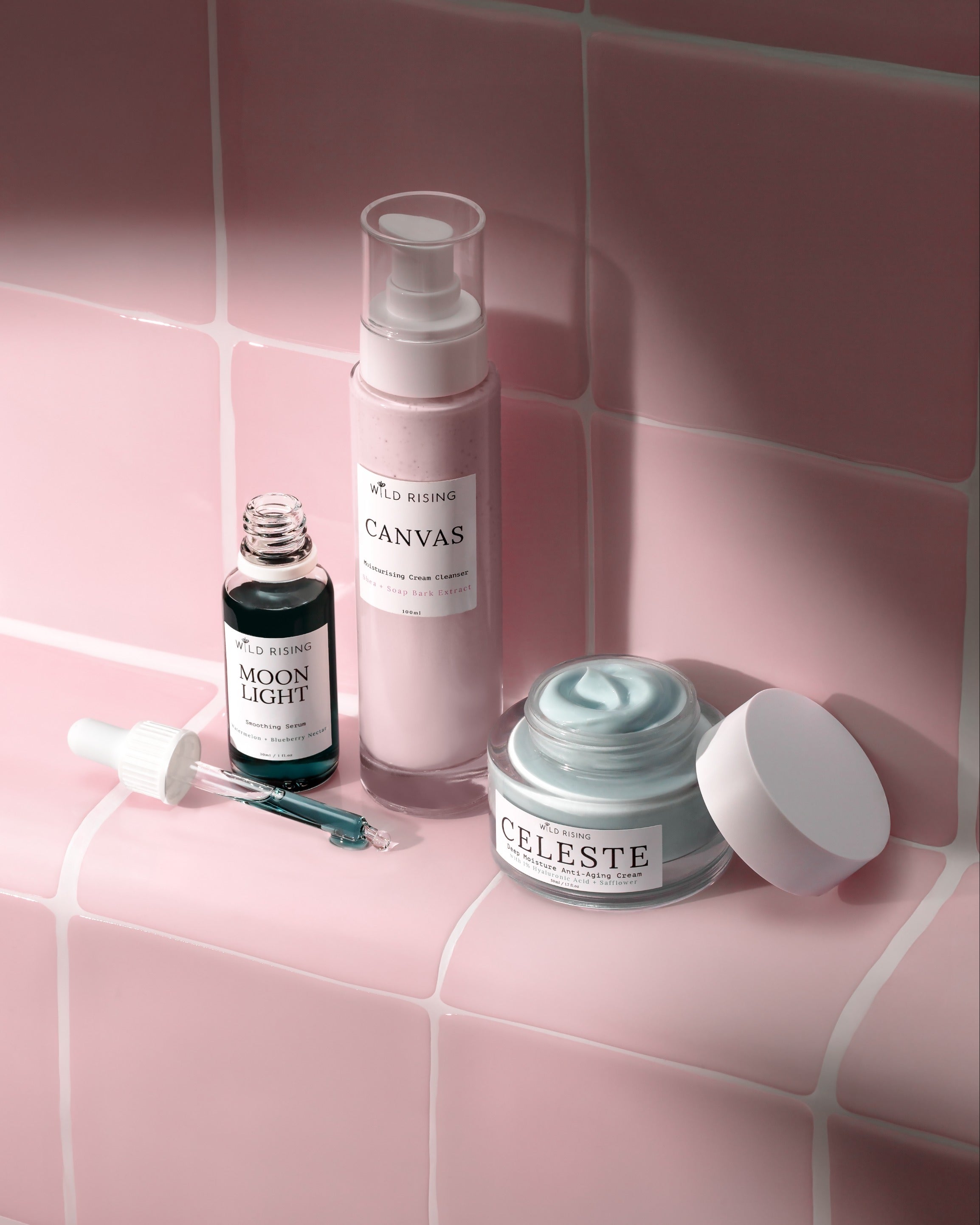 Skincare products including a bottle, jar, and dropper on a pink tiled background