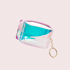 An iridescent holographic cosmetic pouch with a gold keychain ring, shown on a solid pale pink background.