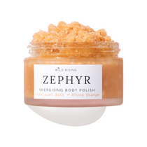 A clear jar of Wild Rising Zephyr Energising Body Polish filled with a peachy-orange granular scrub, shown on a white background with a soft shadow.